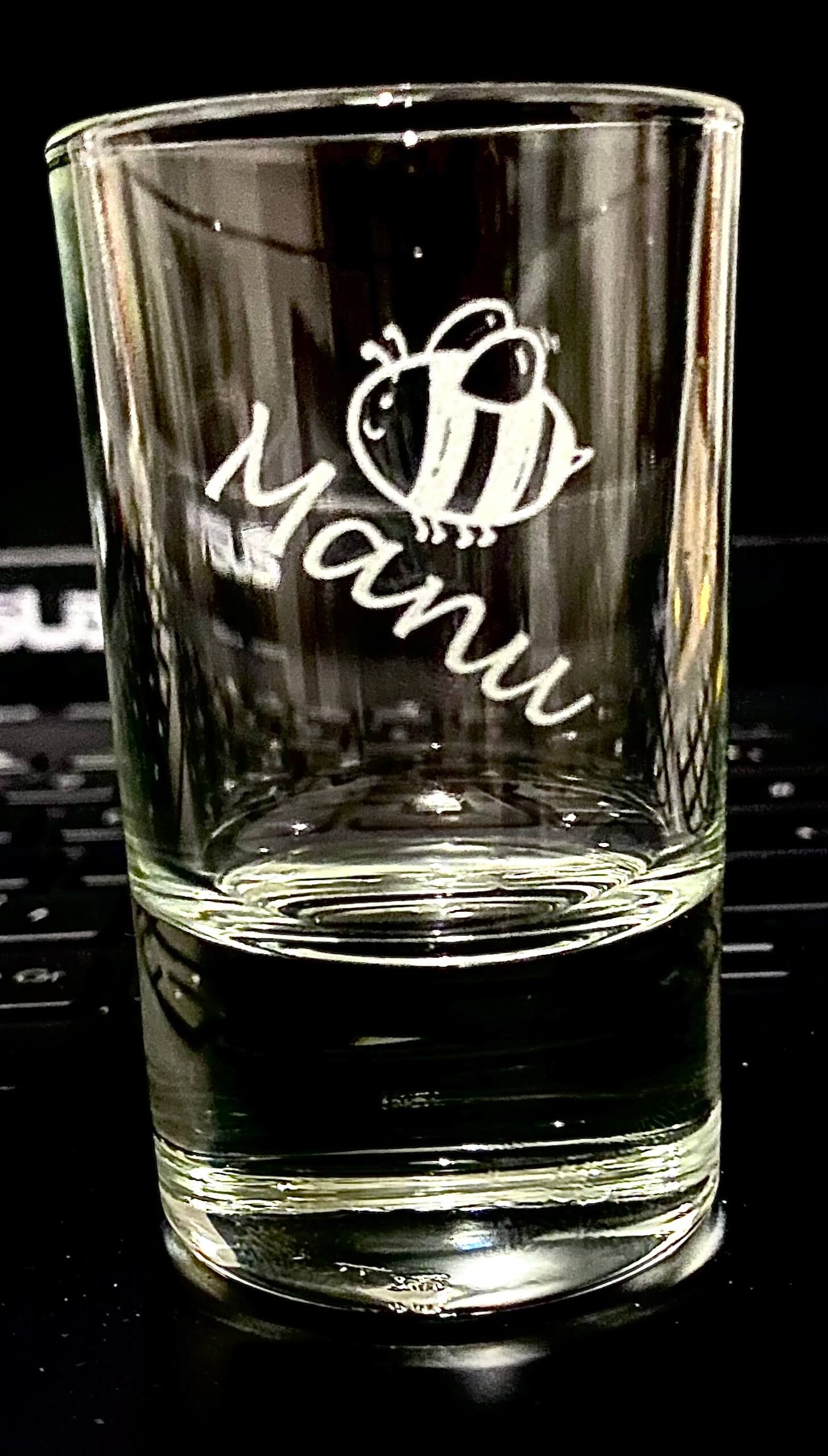 Personalisierter Schnapsglas mit Bienenmotiv und Schriftzug Manu auf schwarzem Hintergrund.