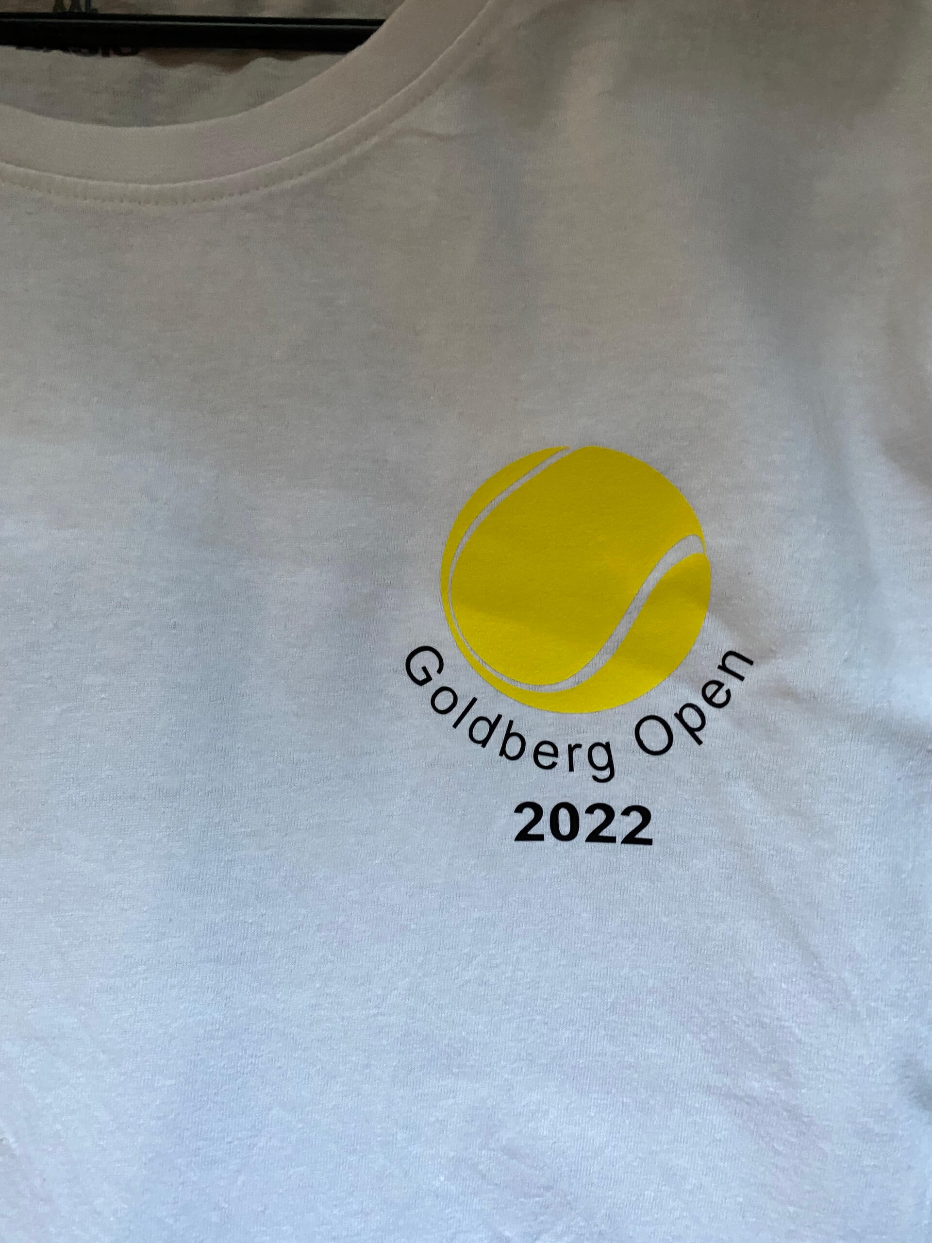 T-Shirt mit Logo der Goldberg Open 2022, Tennisturnier mit gelbem Tennisball-Design auf weißem Hintergrund.