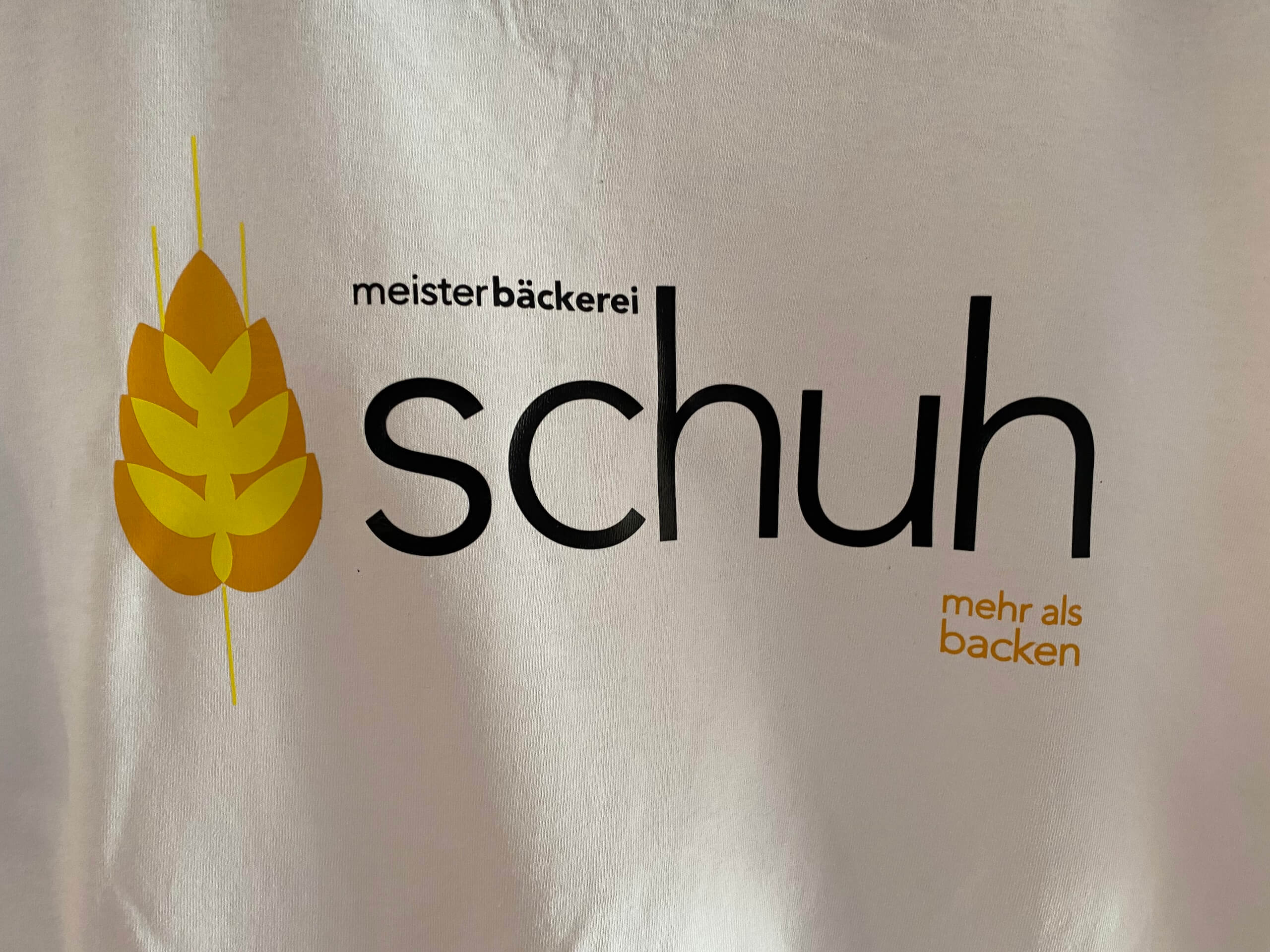 Logo der Meisterbäckerei Schuh mit gelben Ährensymbol, Slogan: mehr als backen.
