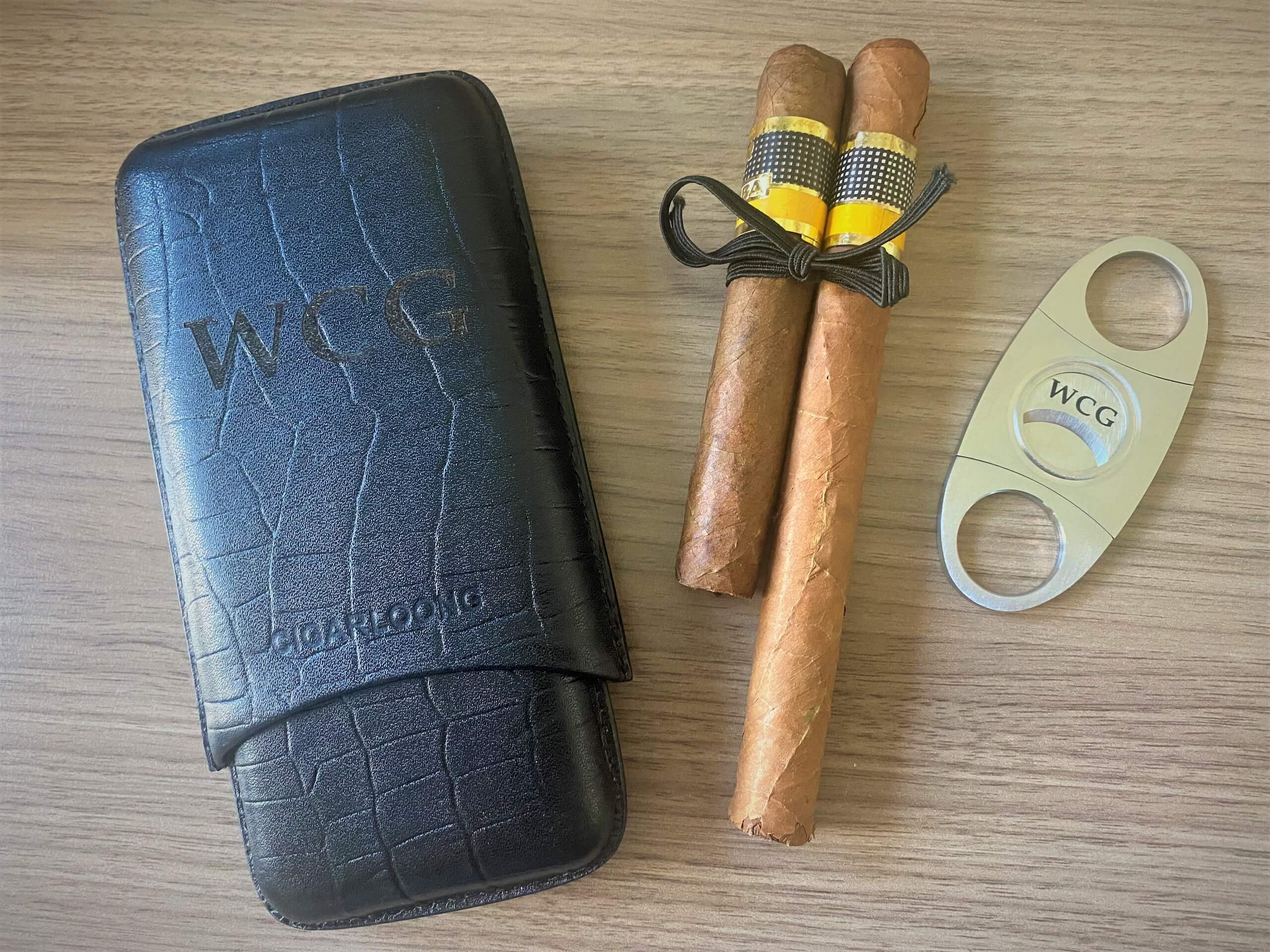 Lederetui, zwei Zigarren mit Banderole und Zigarrenschneider auf Holztisch. Perfekt für Zigarrenliebhaber.