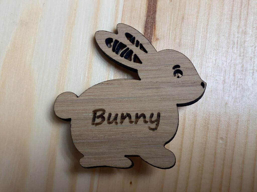 Personalisierter hölzerner Hasenanhänger mit Gravur auf hellem Holzuntergrund.