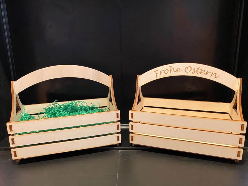 Zwei Holztruhen, eine mit grünem Papier ausgekleidet und eine mit „Frohe Ostern“ Gravur, stehen nebeneinander.