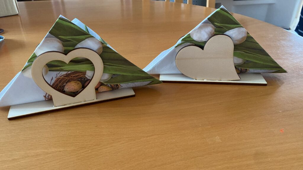 Zwei herzförmige Serviettenhalter aus Holz mit Osterdekoration auf einem Holztisch, ideal als personalisiertes Geschenk.