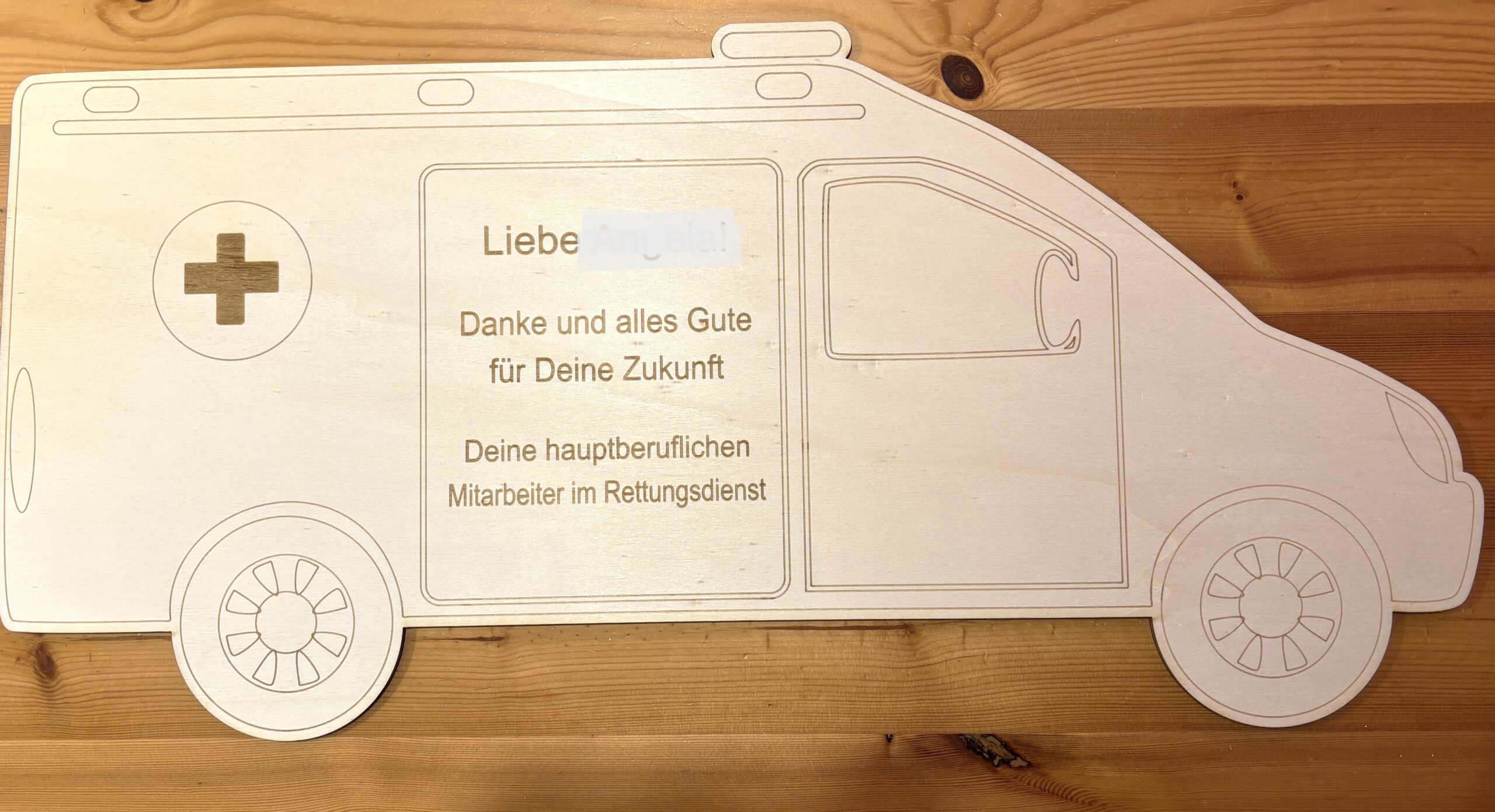 Holz-Ambulanz mit eingraviertem Text: „Danke und alles Gute für Deine Zukunft” von Rettungsdienst-Mitarbeitern.