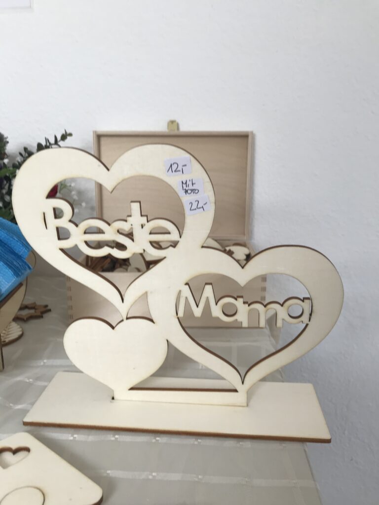 Holzornament mit der Gravur „Beste Mama“ in Herzform auf Tisch, ideale personalisierte Geschenkidee.