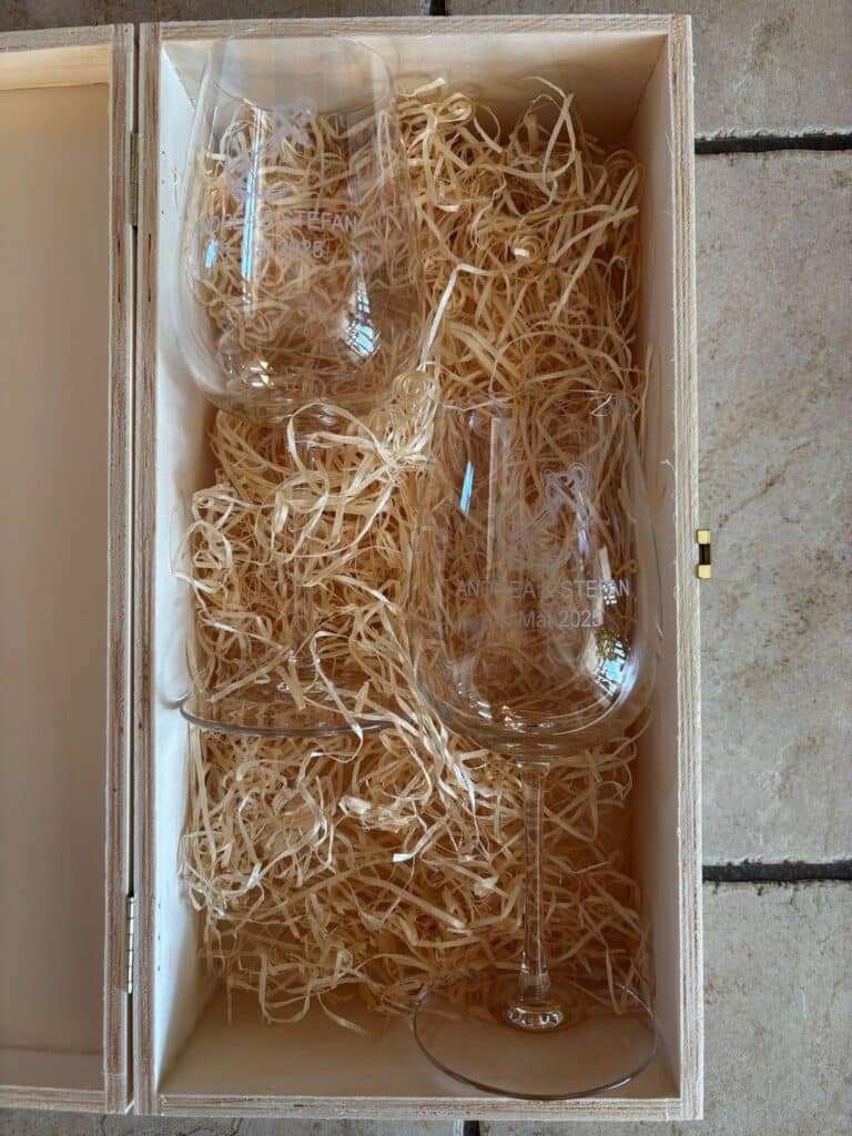 Zwei personalisierte Weingläser mit Gravur in Holzkiste auf Holzwolle gebettet.