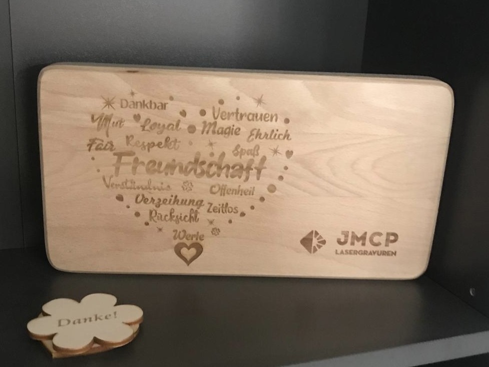 Holzbrett mit gelaserten Wörtern zur Freundschaft, von JMCP Lasergravuren, daneben ein Blumendekor mit „Danke!“.