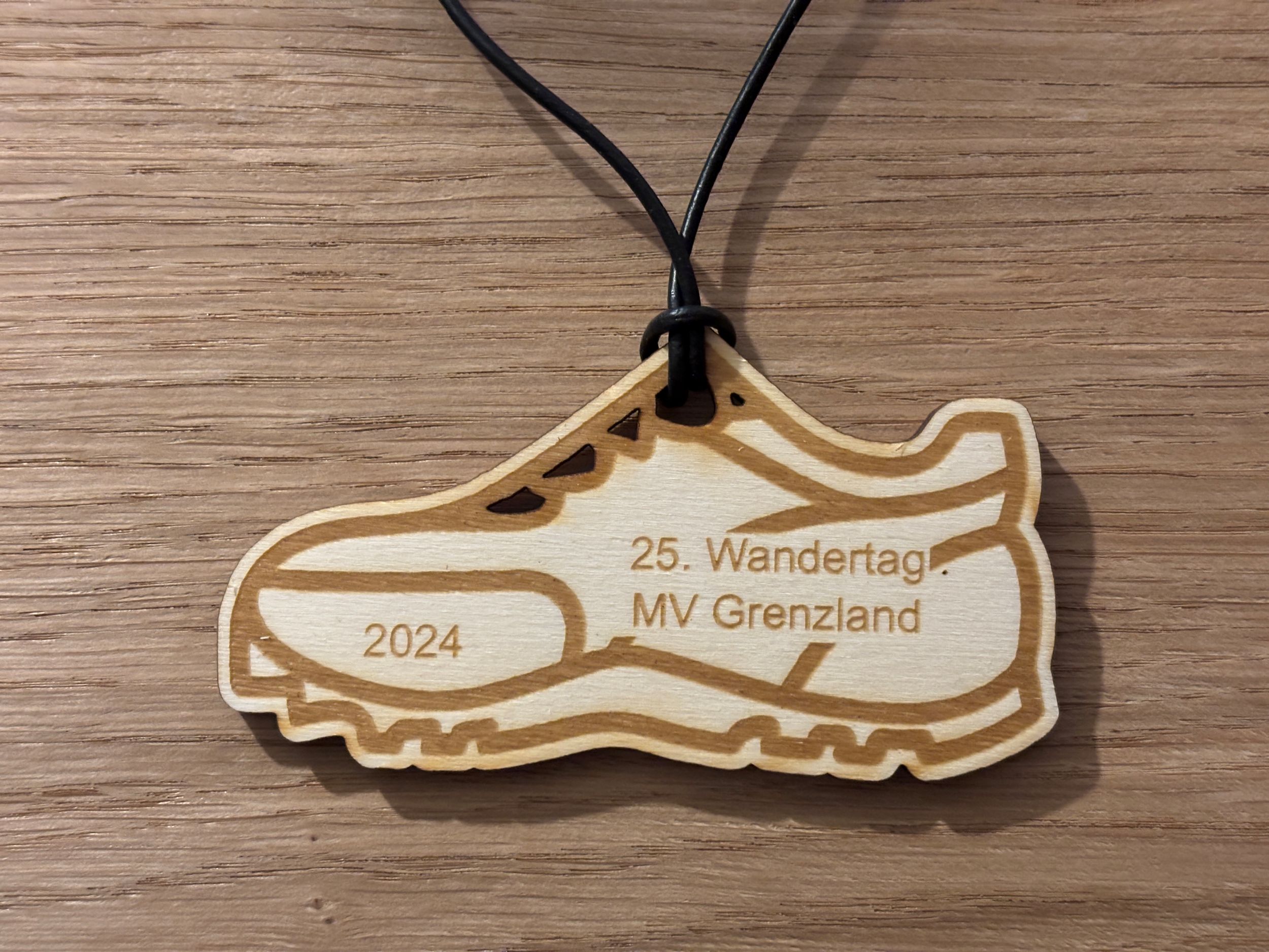 Holzanhänger in Schuhform, beschriftet mit 25. Wandertag MV Grenzland 2024 auf Holztisch liegend.