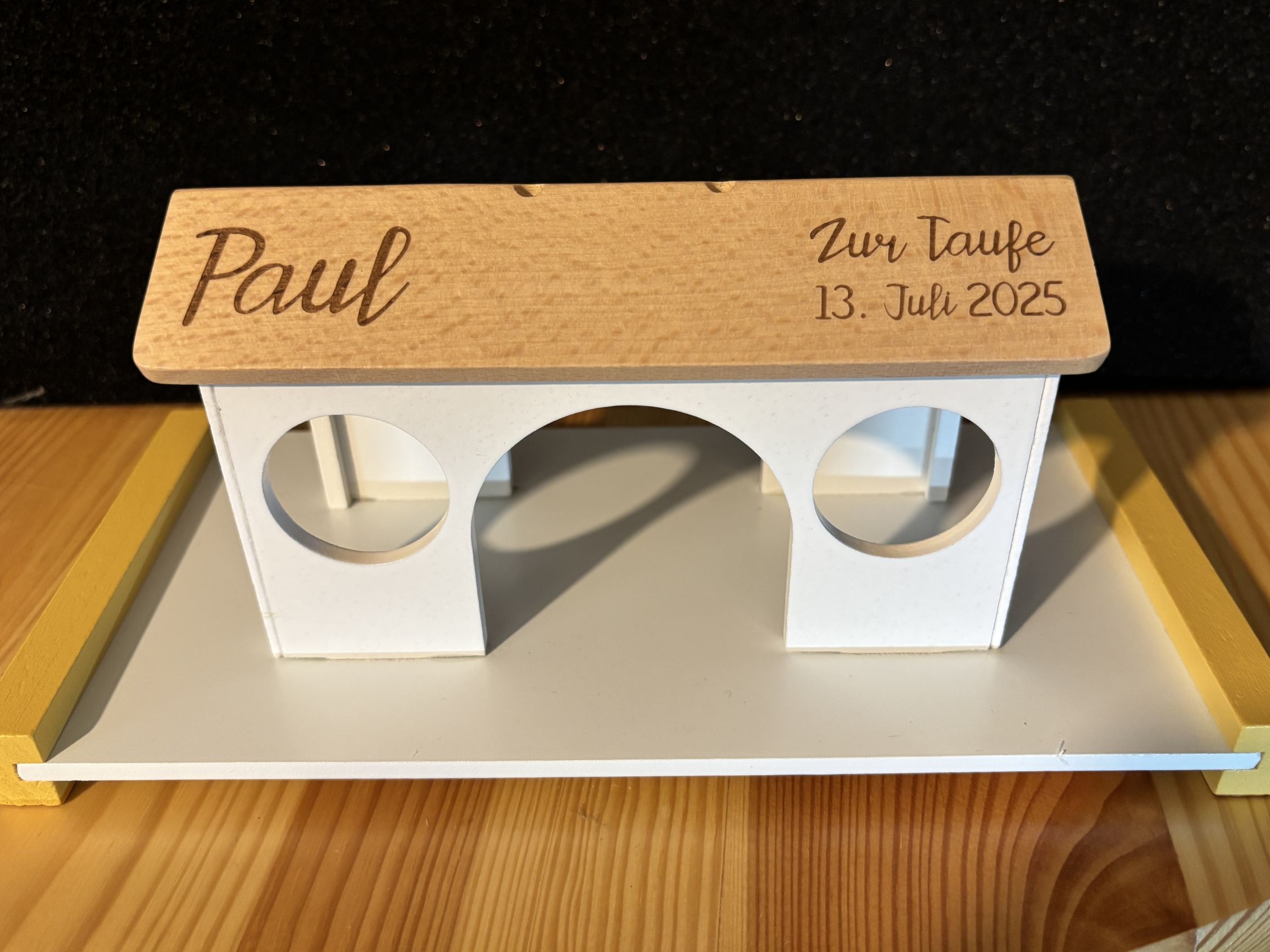 Holz-Deko zur Taufe mit eingraviertem Datum 13. Juli 2025 und dem Namen Paul, auf einem Tisch stehend.