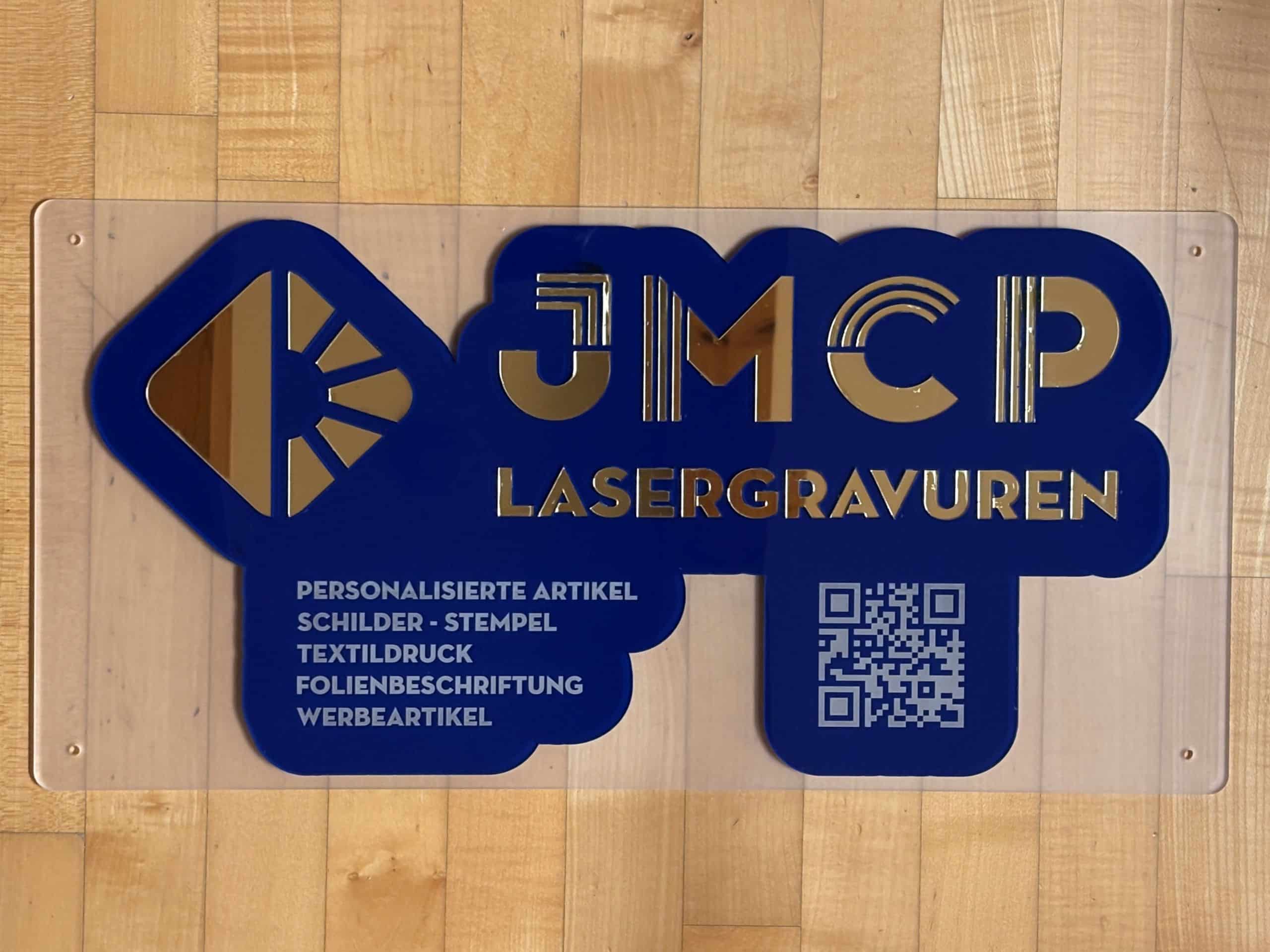 Blaues Firmenschild von JMCP Lasergravuren mit goldenen Buchstaben, QR-Code und Text zu personalisierten Artikeln und Druck.