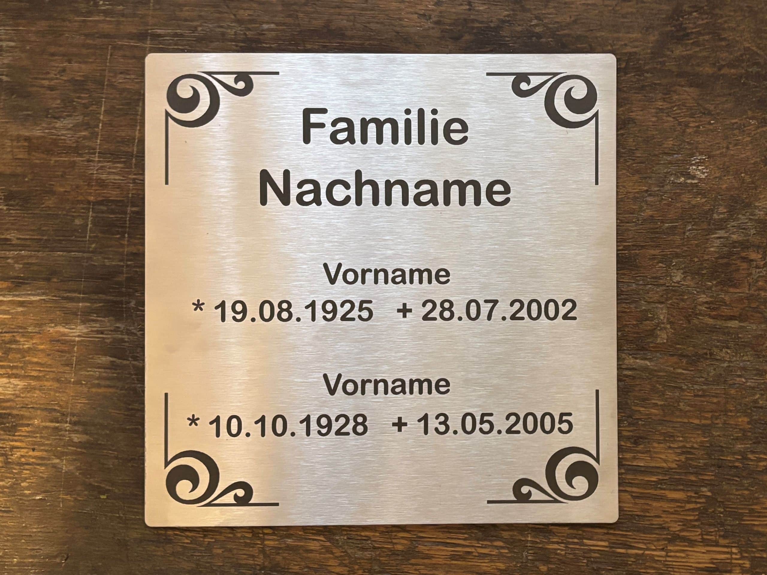 Gravierte Metallplatte mit Verzierungen; enthält Namen und Lebensdaten; für personalisierte Erinnerungsstücke geeignet.