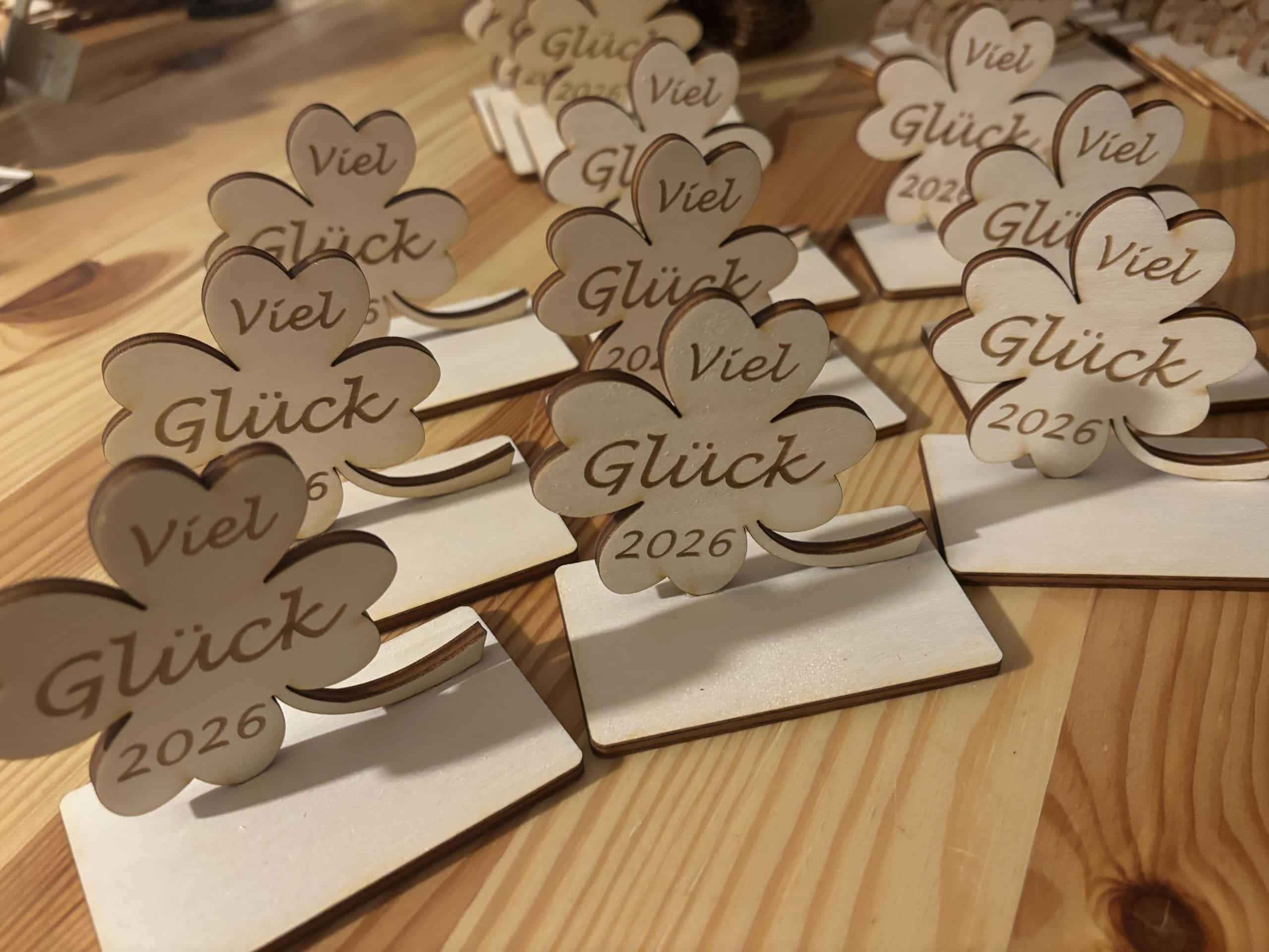 Lasergravierte Kleeblätter mit „Viel Glück 2026“, aus Holz, auf Holztisch arrangiert.