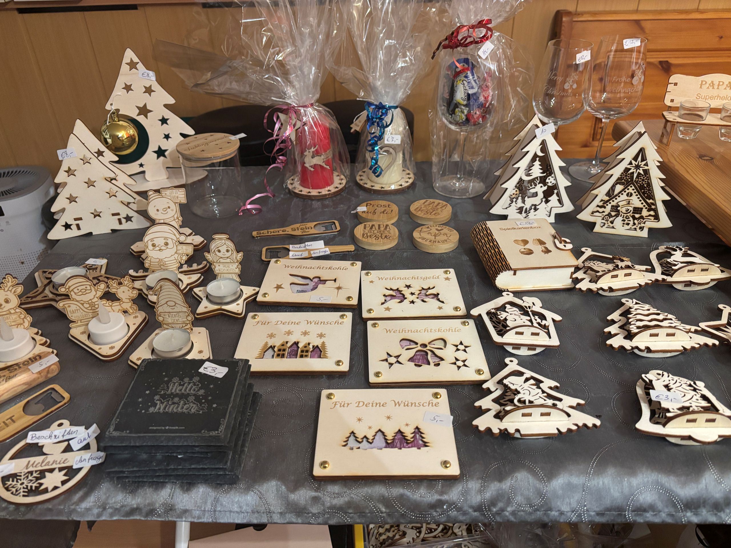 Verschiedene lasergravierte Weihnachtsdekorationen und personalisierte Geschenke auf einem Tisch ausgestellt.