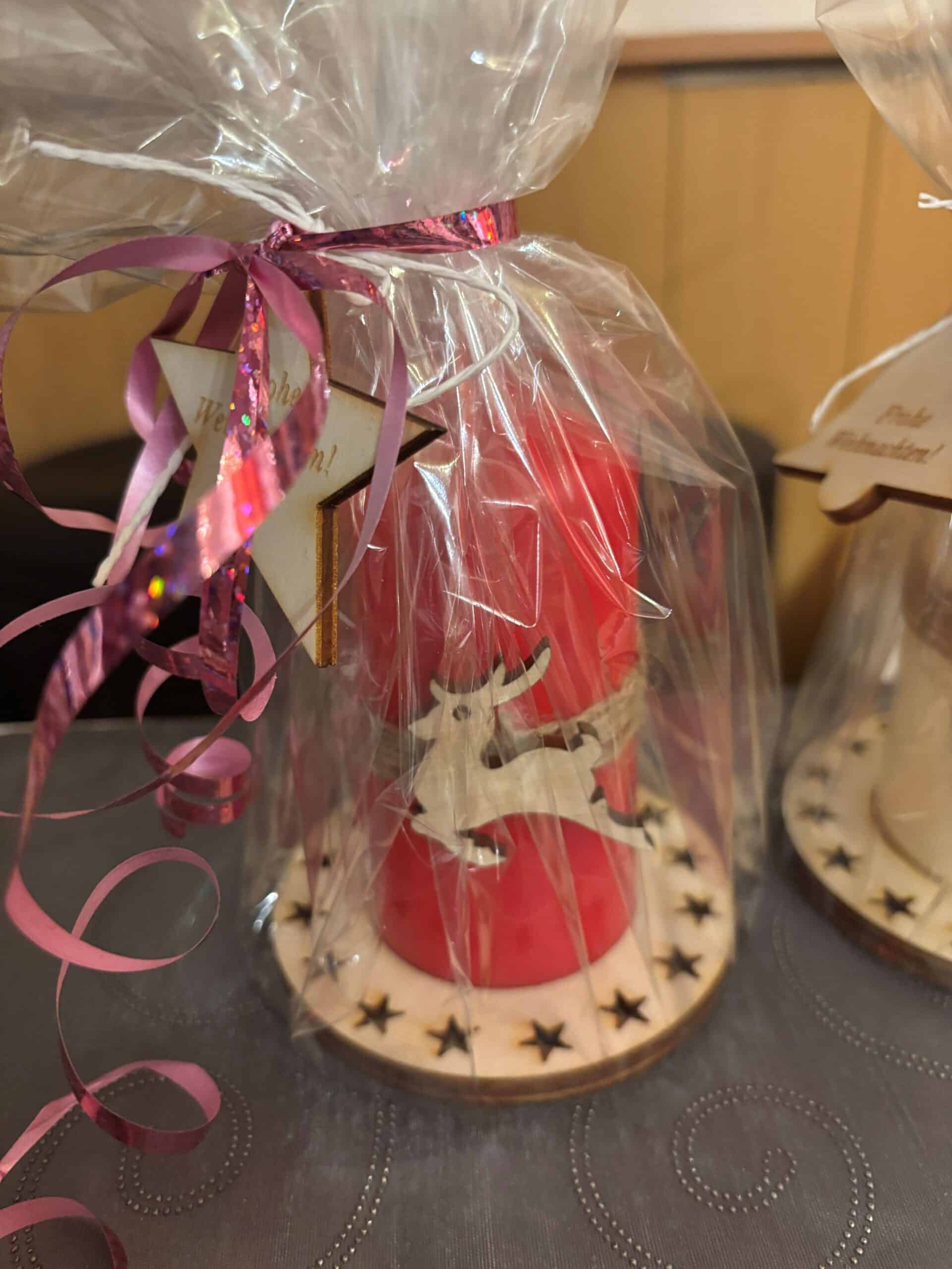Rote Kerze mit Rentiermotiv und Laserschnitt-Sternen, in Folie verpackt, ideal als personalisiertes Geschenk.